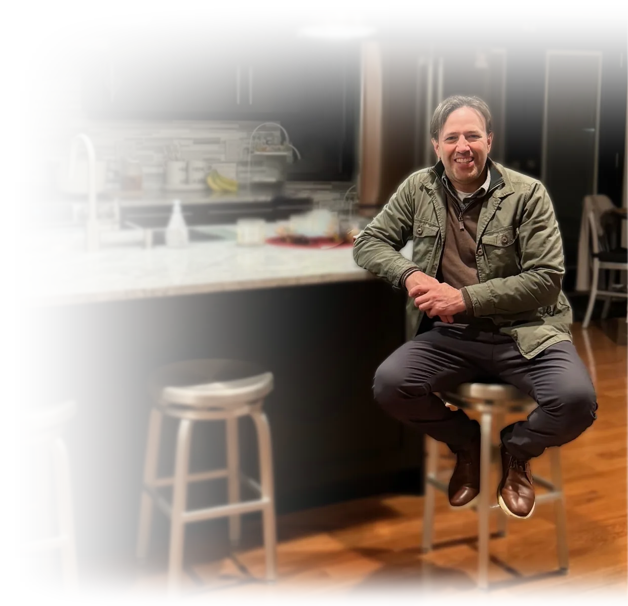 Mike Spina, founder of Spina & Co., seated at a kitchen counter with an open seat beside him